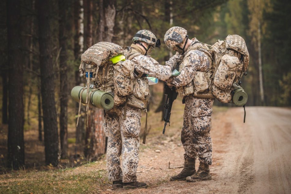 Divi karavīri uz meža ceļa militāro mācību pārgājienā skatās karti