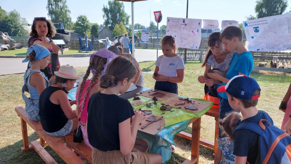 bērni veido priekšmetus no māla laukā pie galda